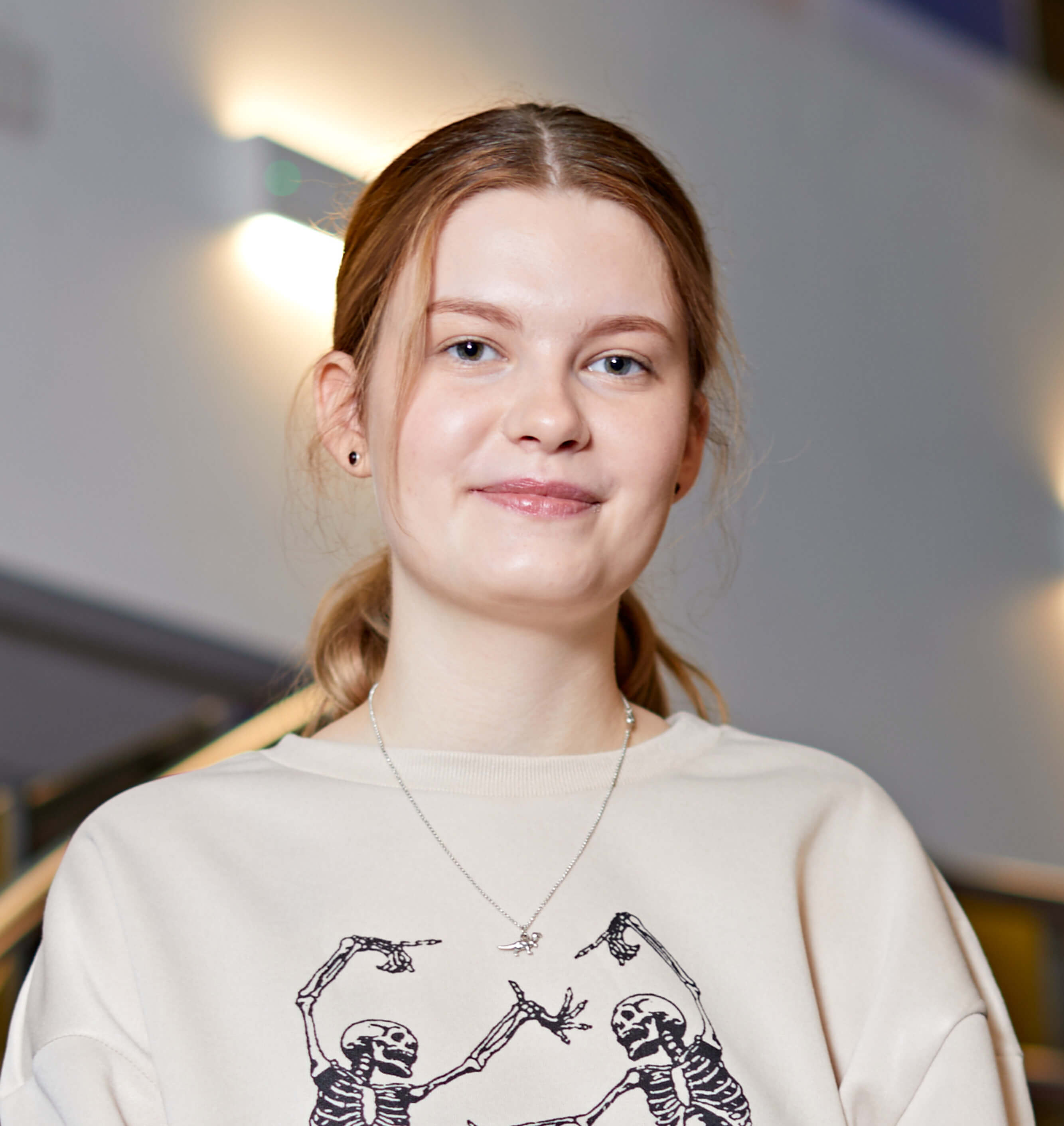 Smiling student standing on staircase, they have grey eyes and auburn hair