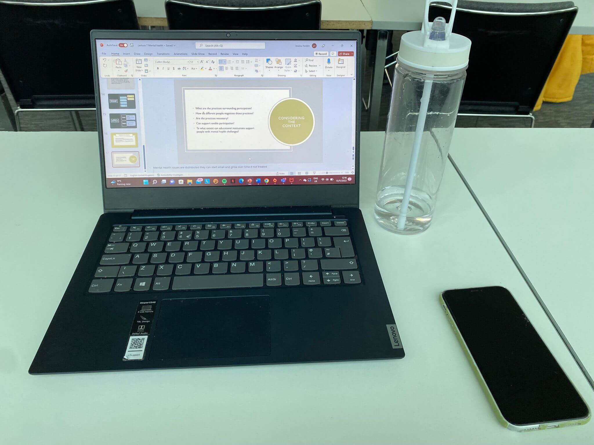 Laptop water bottle and phone on desk taking notes in a lecture