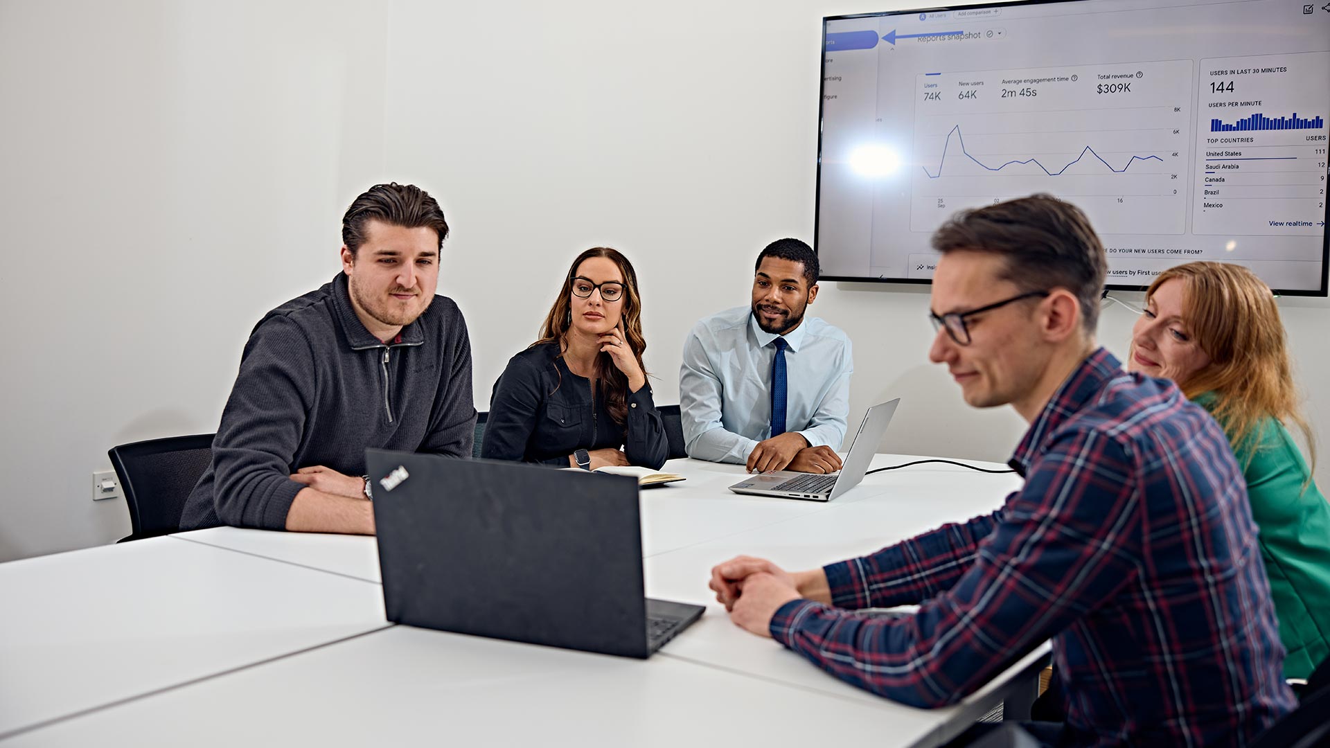 A group of five people in a business meeting, looking at a laptop.