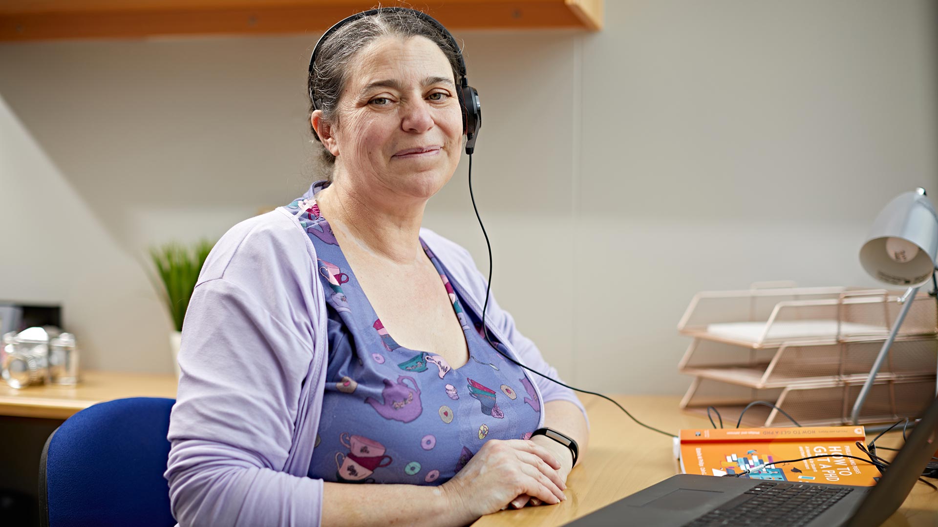 A distance learning student wearing a headset, sat at their desk with a laptop and books.