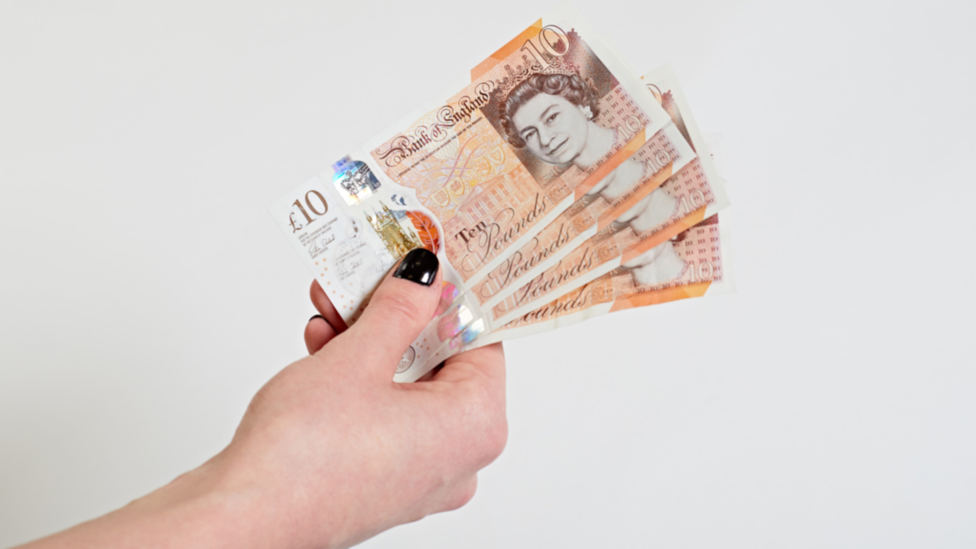 A hand holding several £10 notes