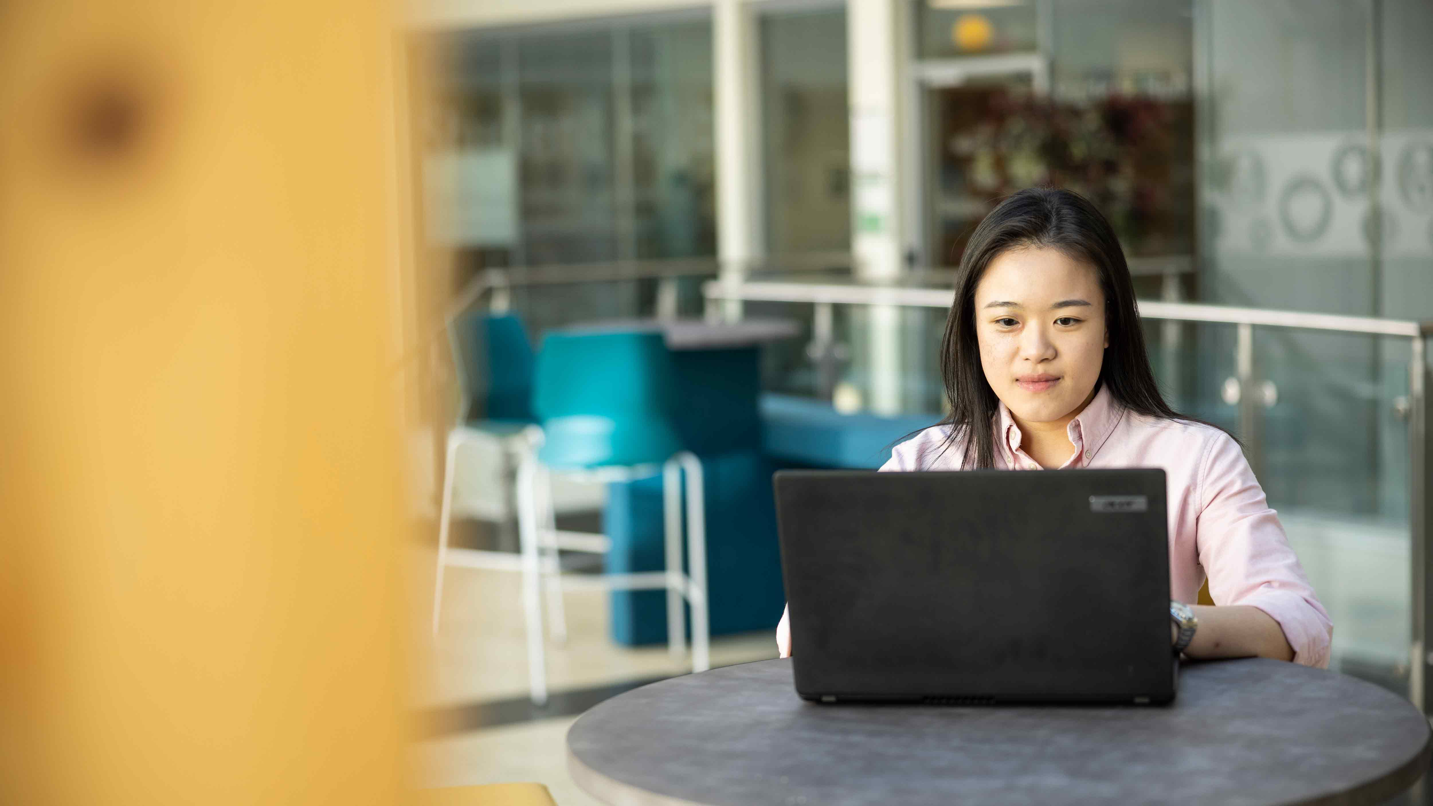 A student sits at a table in the Charles Sikes building at her laptop.