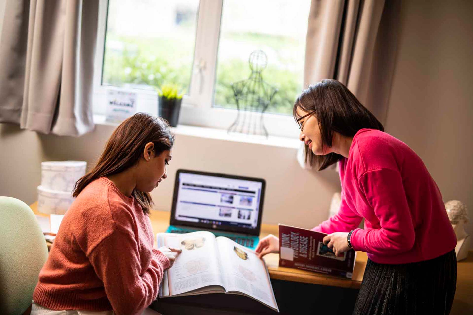 Some students looking over some text next to a laptop in a dorm