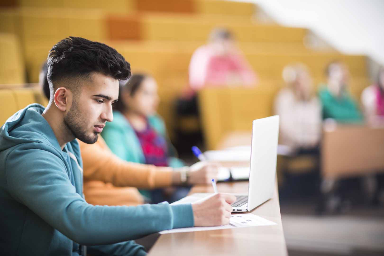 Person with a blue hoodie looking at a laptop whilst in lecture