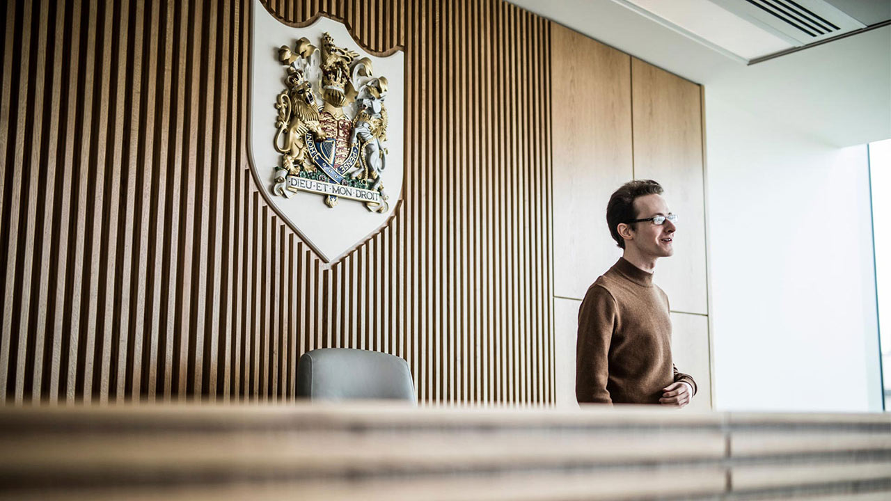 A student in The Oastler Building's Law Courtroom with The Royal Coat of Arms on the wall