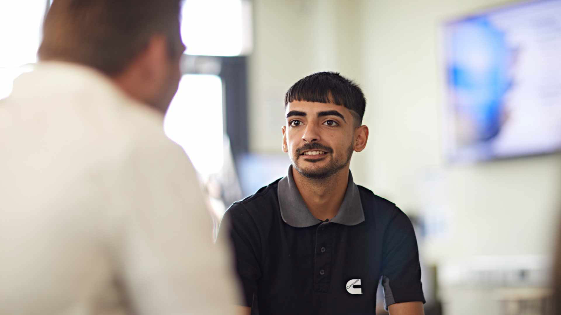 A student apprentice facing the camera as they speak to someone who is blurred to the side of the image.