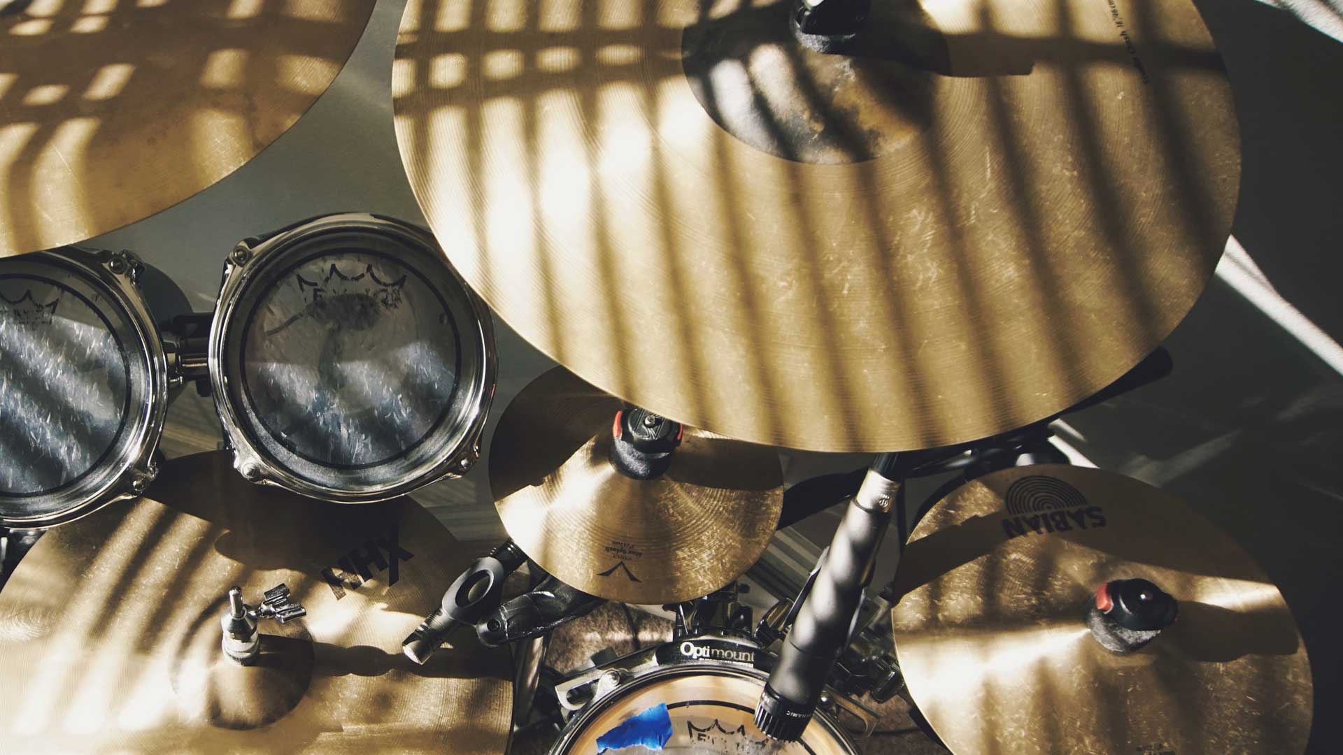 Overhead photo of cymbals on a drum kit. The cymbals are striped by shadows from blinds. 